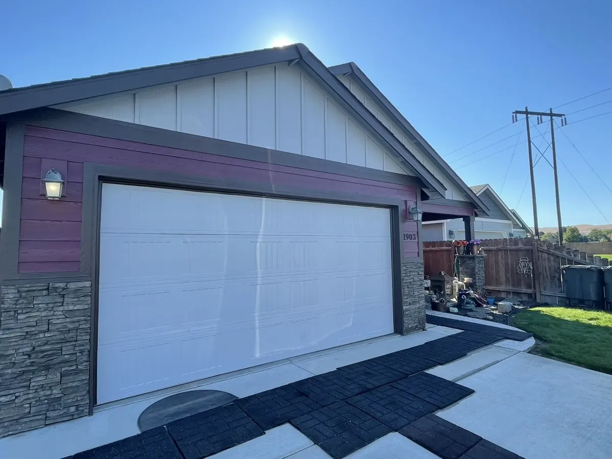 Garage with a burgundy accent colour, board and batten siding and stone veneer